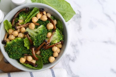 Photo of Delicious salad with shimeji mushrooms, chickpeas and broccoli in bowl on white marble table, top view. Space for text