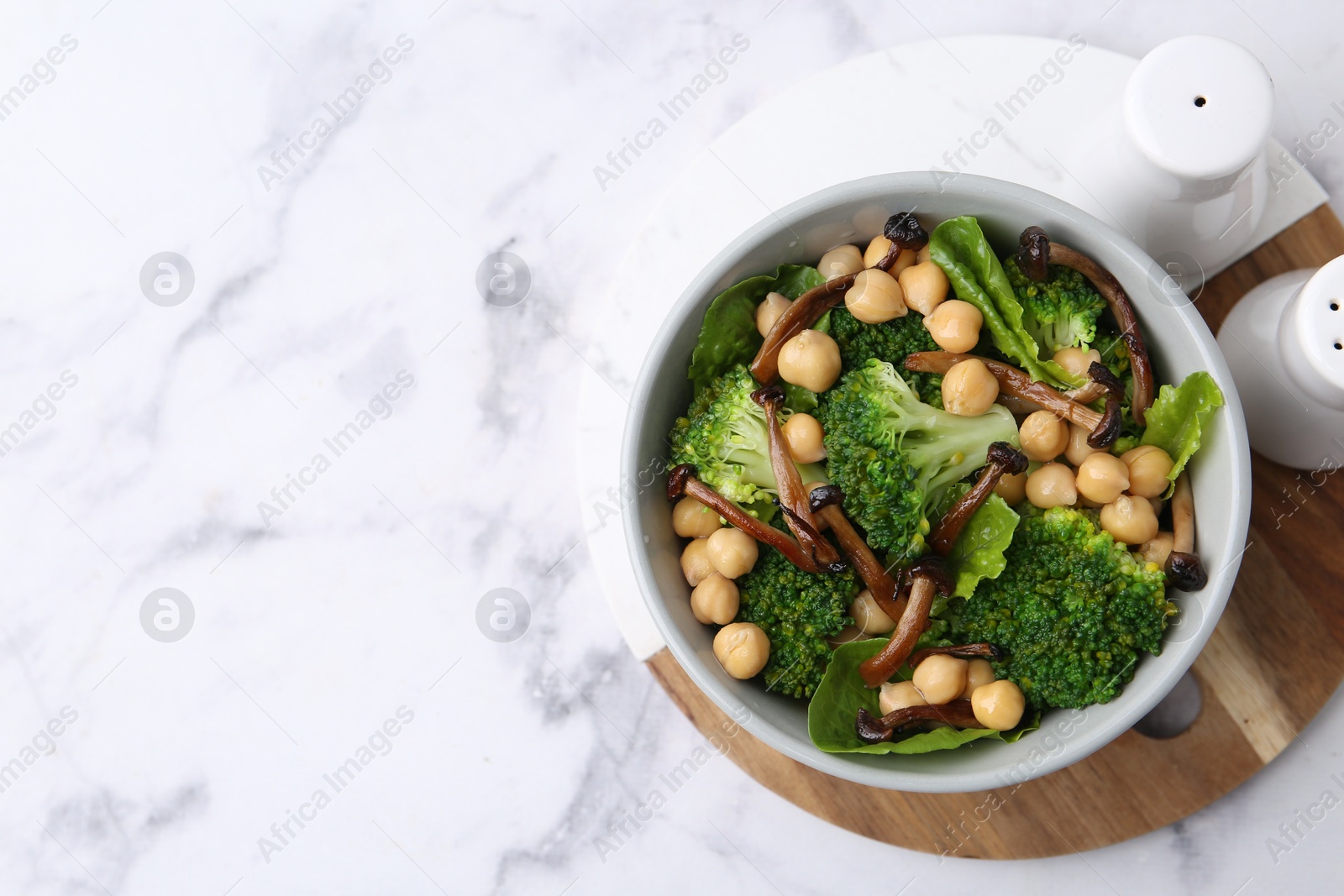 Photo of Delicious salad with shimeji mushrooms, chickpeas and broccoli in bowl on white marble table, top view. Space for text