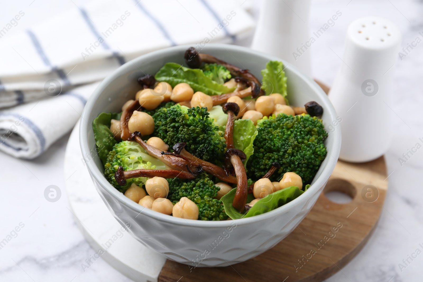 Delicious salad with shimeji mushrooms, chickpeas and broccoli in bowl on white marble table, closeup Photo of Delicious salad with shimeji mushrooms, chickpeas and broccoli in bowl on white marble table, closeup
