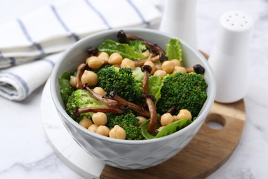 Photo of Delicious salad with shimeji mushrooms, chickpeas and broccoli in bowl on white marble table, closeup