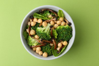 Photo of Delicious salad with shimeji mushrooms, chickpeas and broccoli in bowl on green background, top view