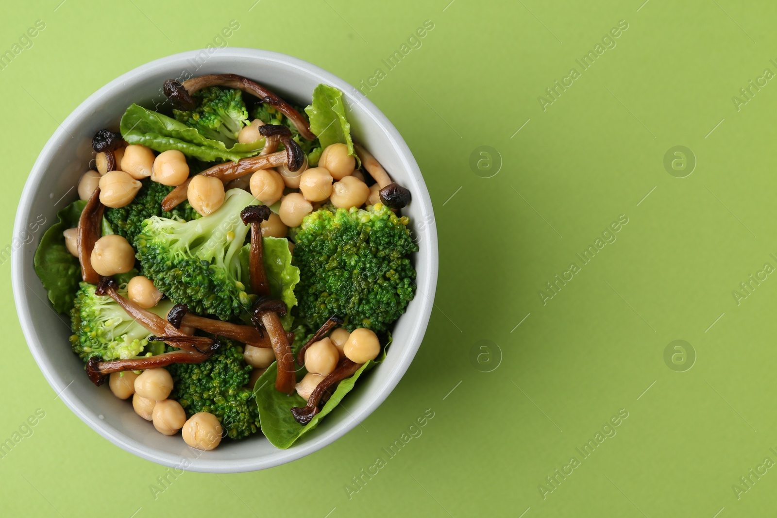 Delicious salad with shimeji mushrooms, chickpeas and broccoli in bowl on green background, top view. Space for text Photo of Delicious salad with shimeji mushrooms, chickpeas and broccoli in bowl on green background, top view. Space for text