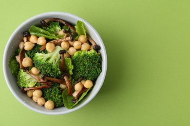 Photo of Delicious salad with shimeji mushrooms, chickpeas and broccoli in bowl on green background, top view. Space for text