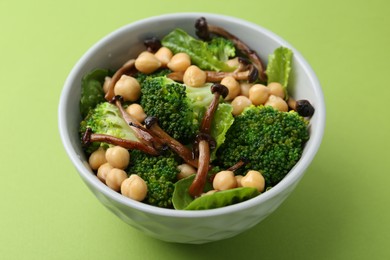 Photo of Delicious salad with shimeji mushrooms, chickpeas and broccoli in bowl on green background, closeup