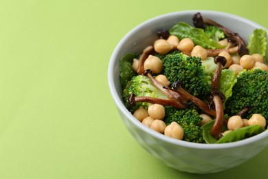 Photo of Delicious salad with shimeji mushrooms, chickpeas and broccoli in bowl on green background, closeup. Space for text
