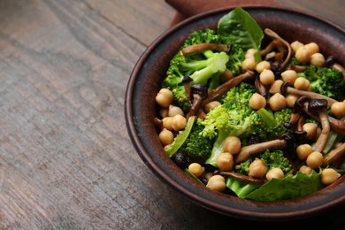 Photo of Delicious salad with shimeji mushrooms, chickpeas and broccoli in bowl on wooden table, closeup. Space for text