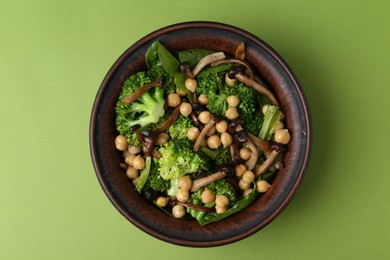 Photo of Delicious salad with shimeji mushrooms, chickpeas and broccoli in bowl on green background, top view