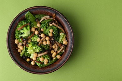 Photo of Delicious salad with shimeji mushrooms, chickpeas and broccoli in bowl on green background, top view. Space for text