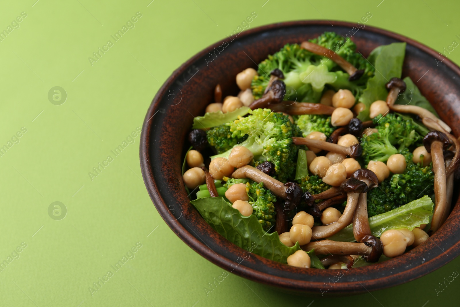 Delicious salad with shimeji mushrooms, chickpeas and broccoli in bowl on green background, closeup. Space for text Photo of Delicious salad with shimeji mushrooms, chickpeas and broccoli in bowl on green background, closeup. Space for text