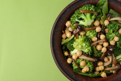 Photo of Delicious salad with shimeji mushrooms, chickpeas and broccoli in bowl on green background, top view. Space for text