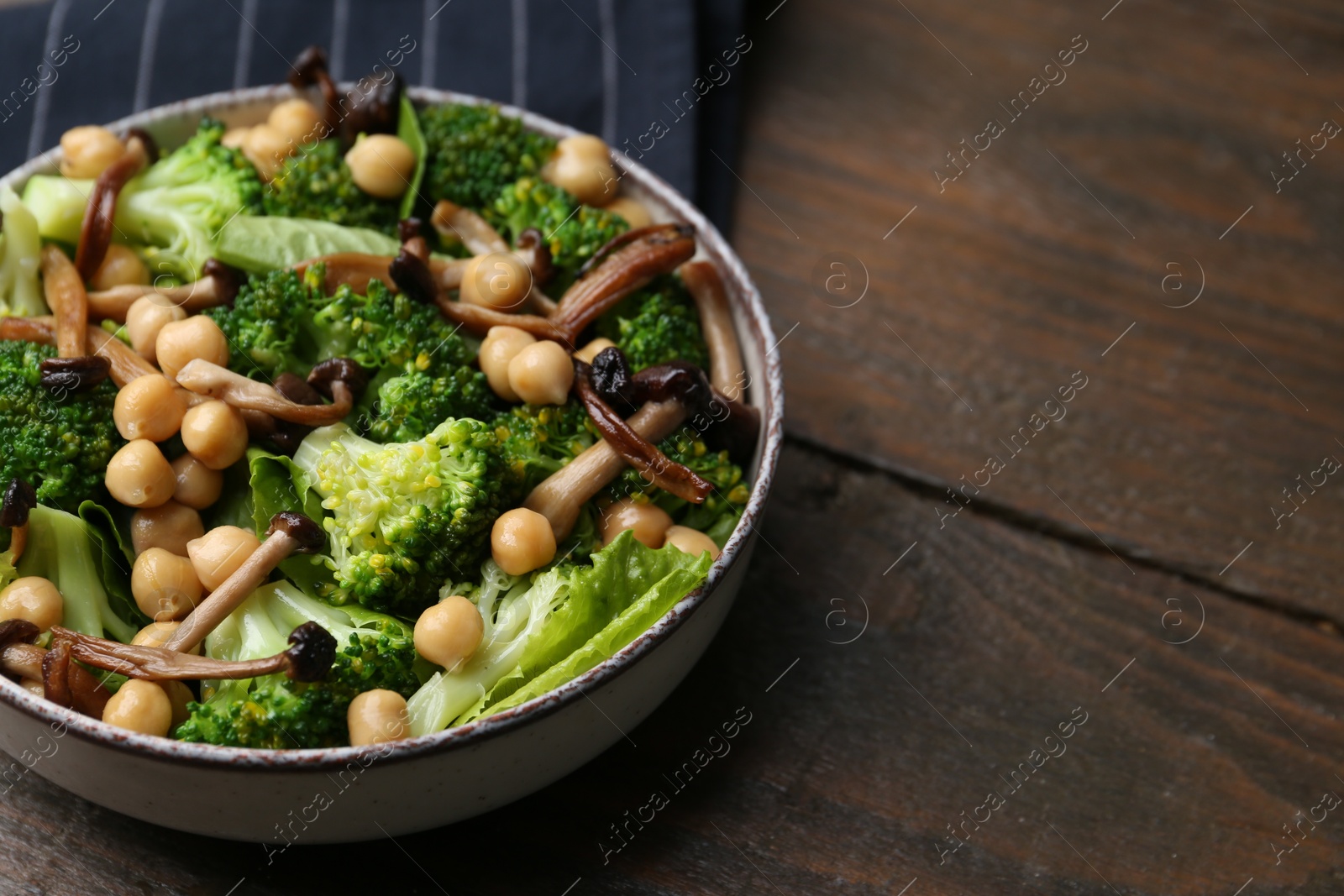 Delicious salad with shimeji mushrooms, chickpeas and broccoli in bowl on wooden table, closeup. Space for text Photo of Delicious salad with shimeji mushrooms, chickpeas and broccoli in bowl on wooden table, closeup. Space for text