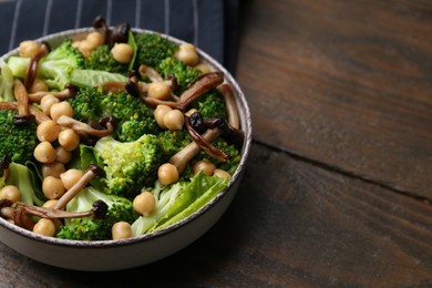 Photo of Delicious salad with shimeji mushrooms, chickpeas and broccoli in bowl on wooden table, closeup. Space for text