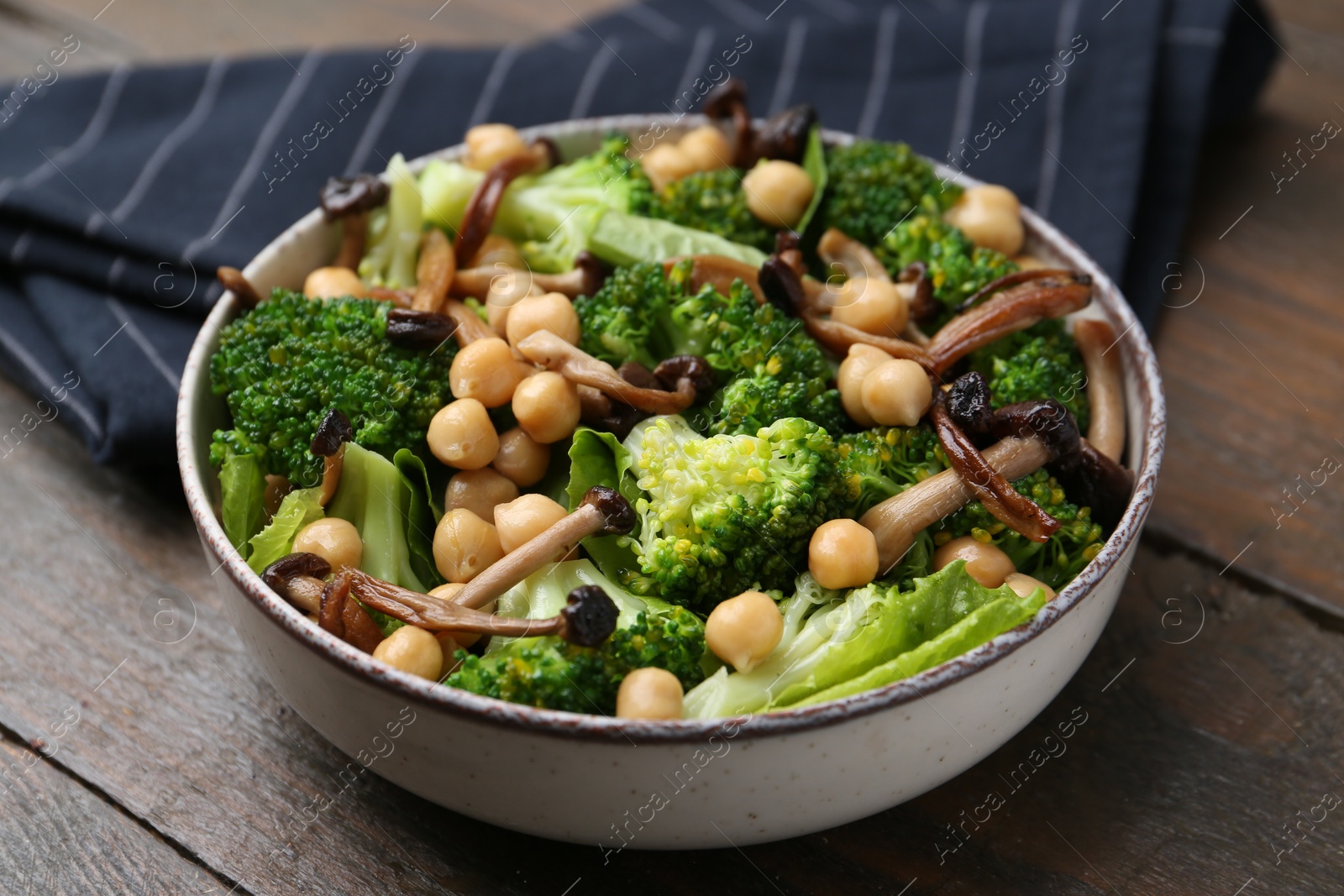 Photo of Delicious salad with shimeji mushrooms, chickpeas and broccoli in bowl on wooden table, closeup