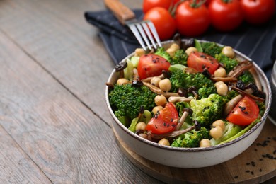 Photo of Delicious salad with shimeji mushrooms, chickpeas, tomatoes and broccoli on wooden table, closeup. Space for text