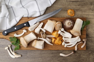 Photo of Different raw mushrooms, parsley and knife on wooden table, flat lay