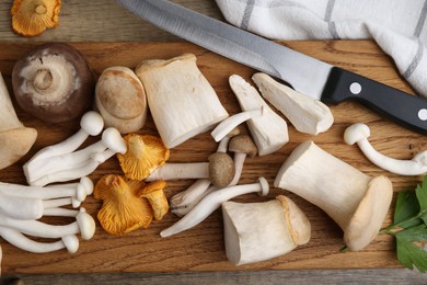 Photo of Different raw mushrooms and knife on wooden table, flat lay
