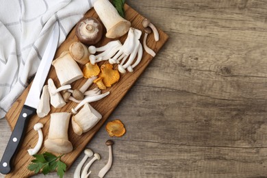 Photo of Different raw mushrooms, parsley and knife on wooden table, flat lay. Space for text