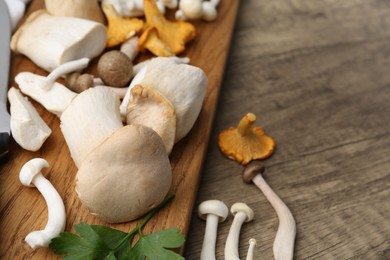 Photo of Different raw mushrooms and parsley on wooden table, closeup. Space for text