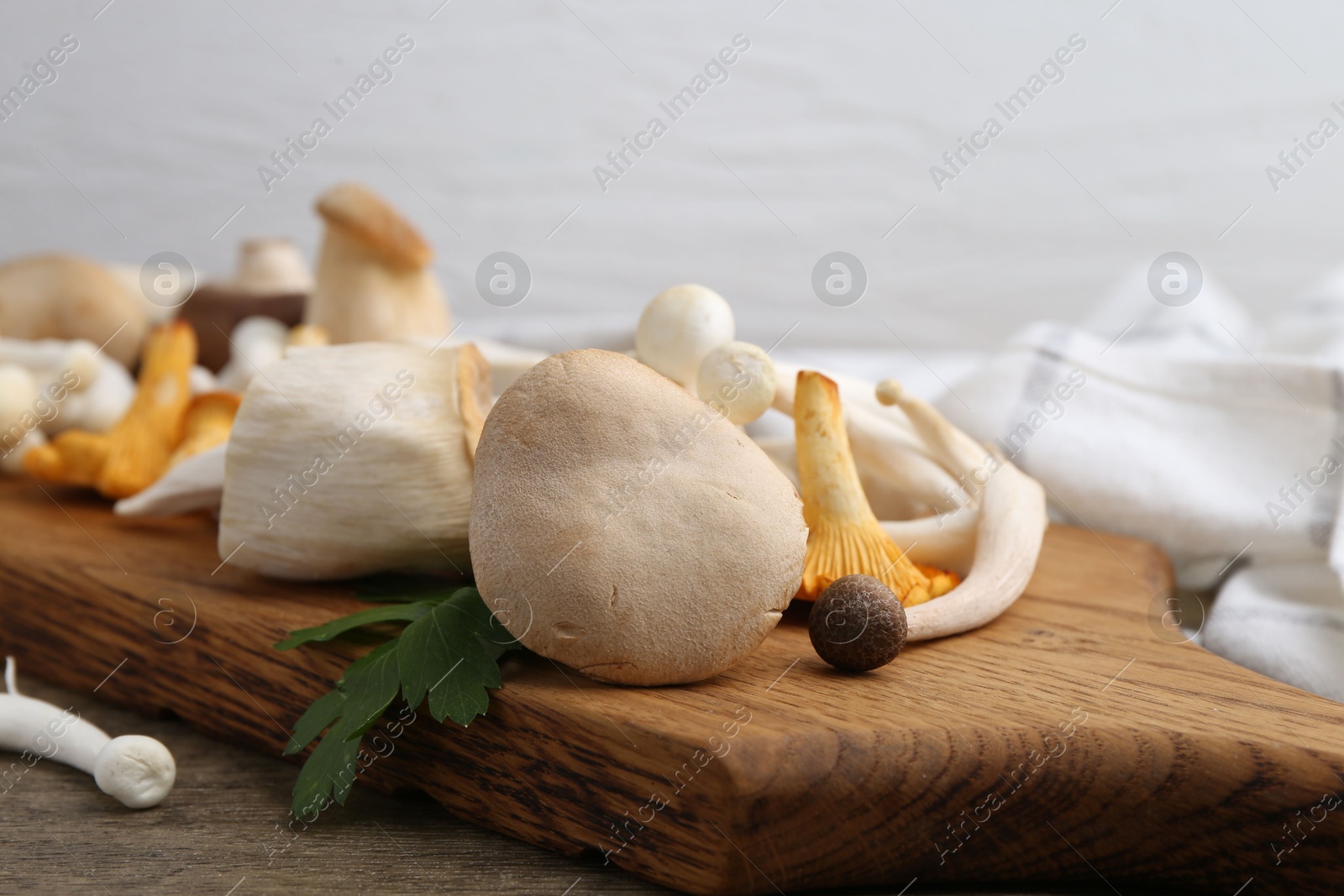 Different raw mushrooms and parsley on wooden table against light background, closeup Photo of Different raw mushrooms and parsley on wooden table against light background, closeup