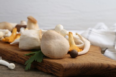Photo of Different raw mushrooms and parsley on wooden table against light background, closeup