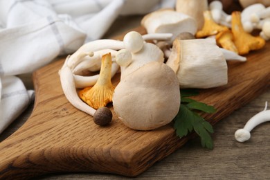 Photo of Different raw mushrooms and parsley on wooden table, closeup