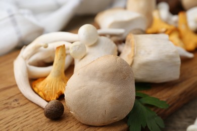 Photo of Different raw mushrooms and parsley on wooden table, closeup
