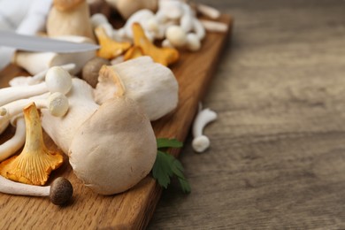 Photo of Different raw mushrooms and parsley on wooden table, closeup. Space for text