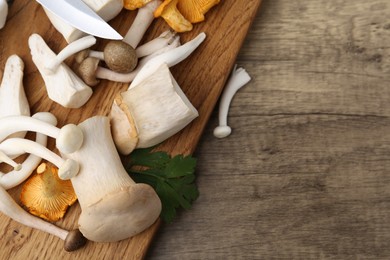 Photo of Different raw mushrooms and parsley on wooden table, flat lay. Space for text