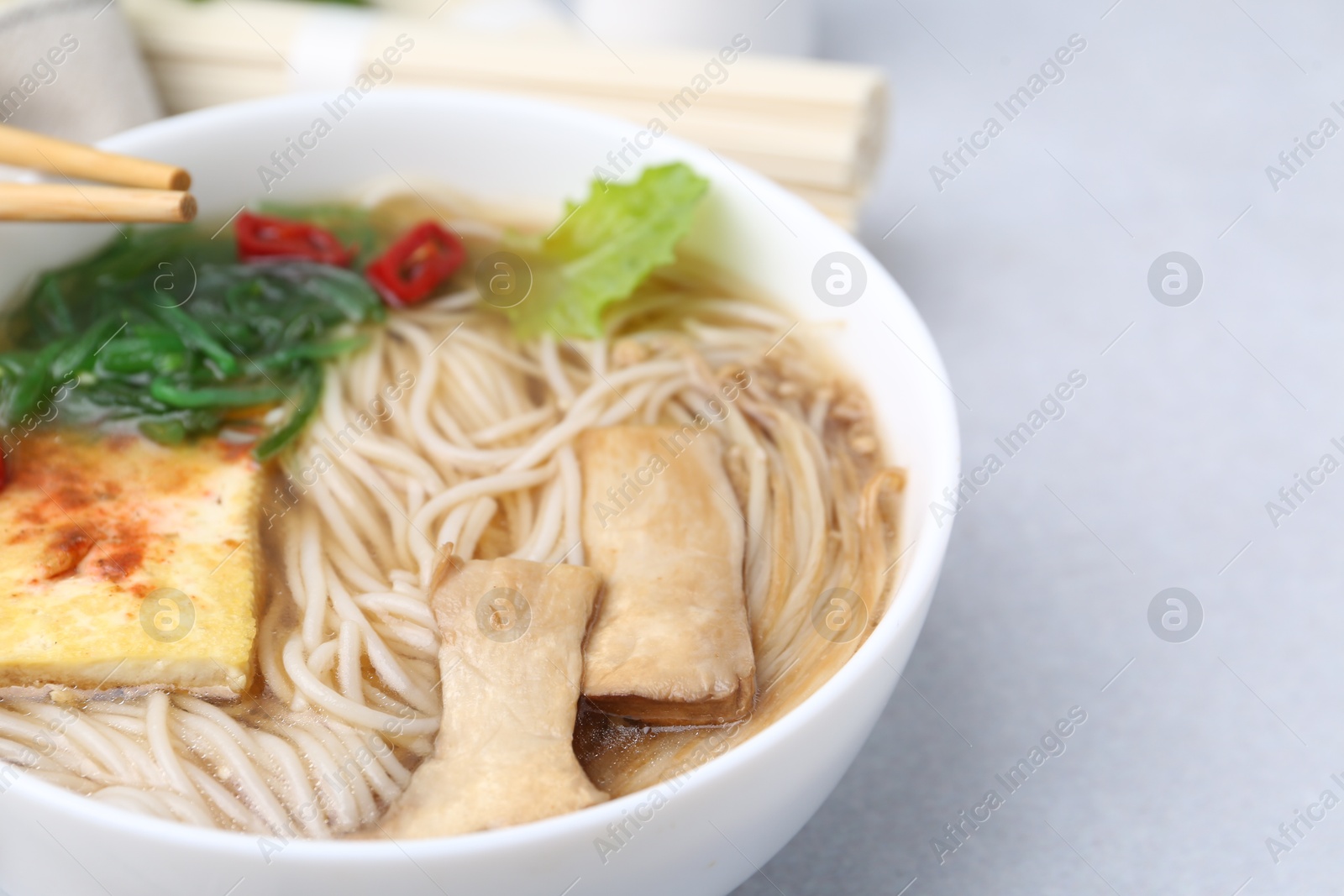 Tasty ramen with enoki and king oyster (eryngii) mushrooms on white table Photo of Tasty ramen with enoki and king oyster (eryngii) mushrooms on white table