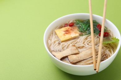 Photo of Tasty ramen with enoki and king oyster (eryngii) mushrooms on green background, closeup. Space for text