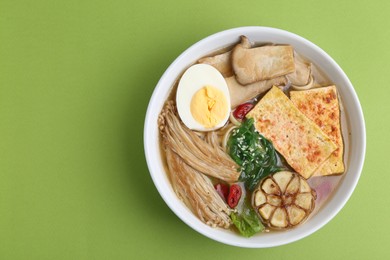 Photo of Tasty ramen with enoki and king oyster (eryngii) mushrooms on green background, top view. Space for text