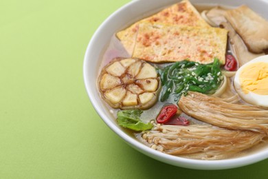 Photo of Tasty ramen with enoki and king oyster (eryngii) mushrooms on green background, closeup. Space for text