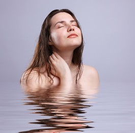 Image of Beautiful young woman with perfect skin against grey background. Her reflection in rippled water