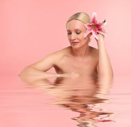 Image of Beautiful woman with perfect skin and lily flower against pink background. Her reflection in rippled water