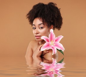 Image of Beautiful woman with perfect skin and lily flower against pale brown background. Her reflection in rippled water
