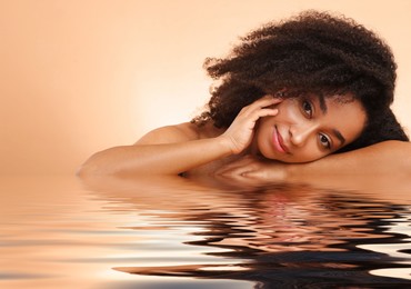 Image of Beautiful woman with perfect skin against pale brown background. Her reflection in rippled water
