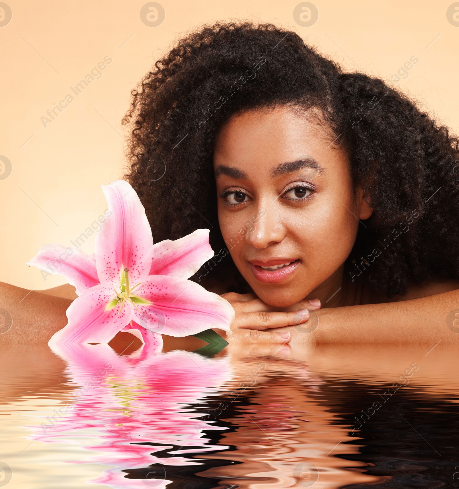 Image of Beautiful woman with perfect skin and lily flower against dark beige background. Her reflection in rippled water