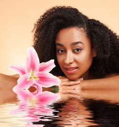 Image of Beautiful woman with perfect skin and lily flower against dark beige background. Her reflection in rippled water