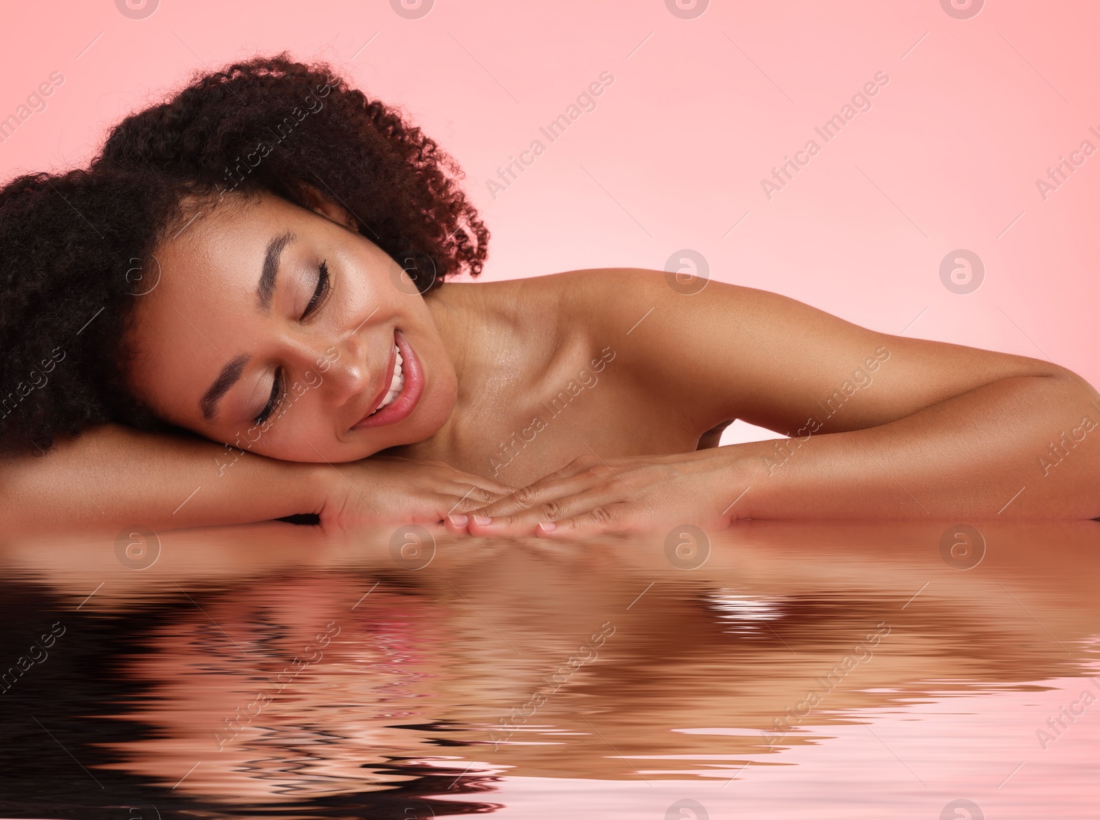 Image of Beautiful woman with perfect skin against pink background. Her reflection in rippled water