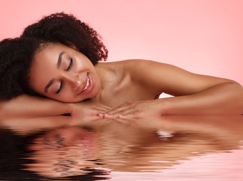 Image of Beautiful woman with perfect skin against pink background. Her reflection in rippled water