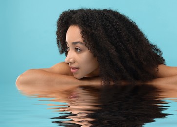 Image of Beautiful woman with perfect skin against light blue background. Her reflection in rippled water