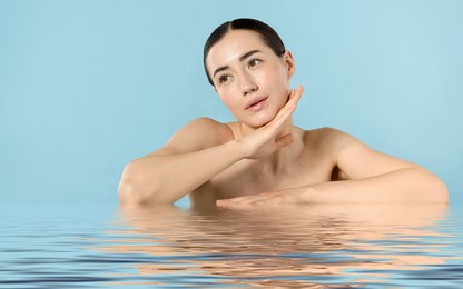 Image of Beautiful woman with perfect skin against light blue background. Her reflection in rippled water