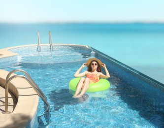 Image of Girl with inflatable ring resting in swimming pool at sea resort