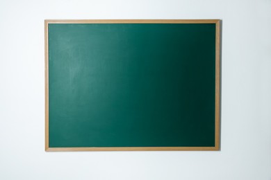 Photo of Blank green chalkboard on white wall indoors