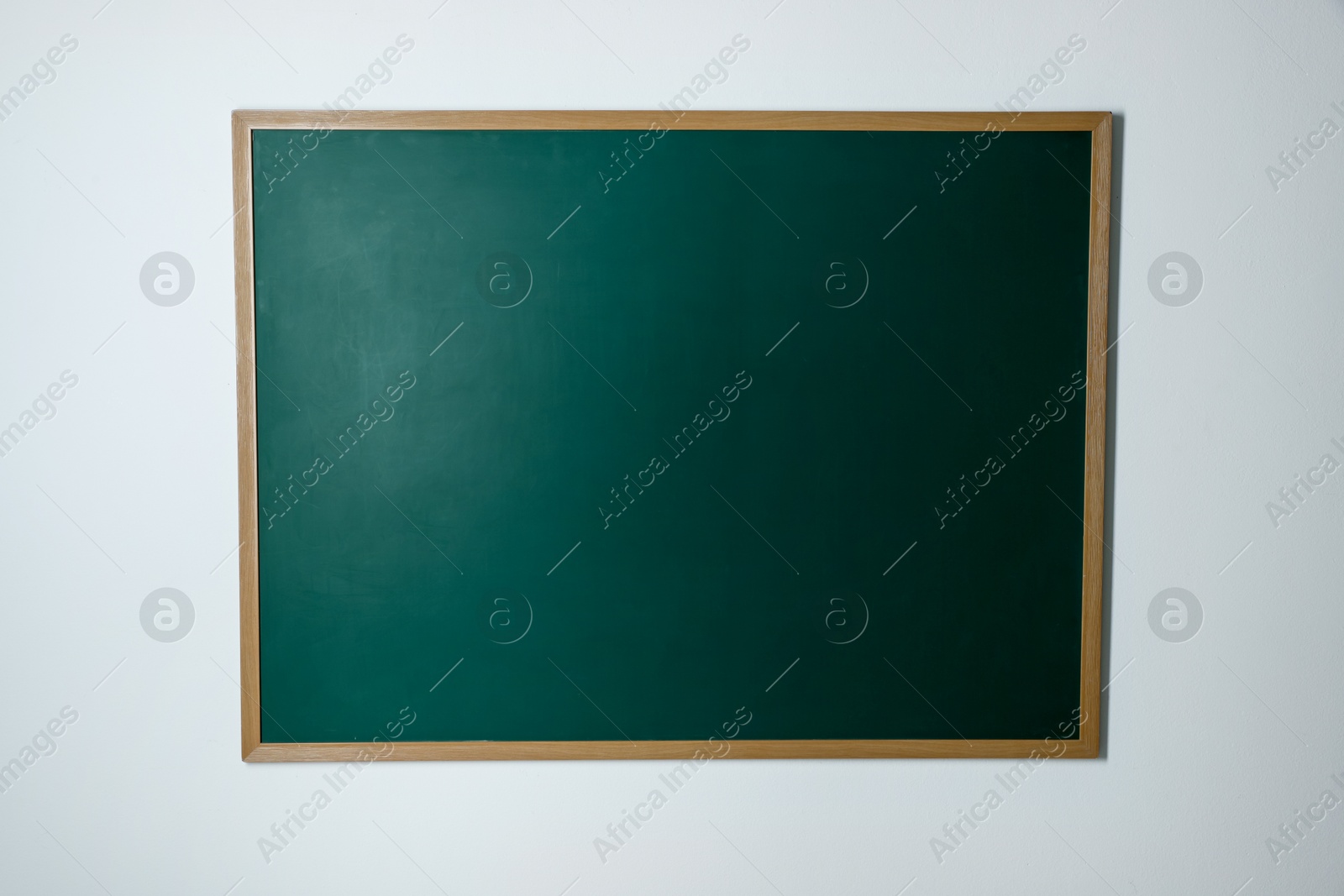 Photo of Blank green chalkboard on white wall indoors