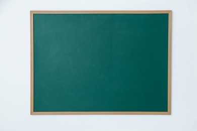 Photo of Blank green chalkboard on white wall indoors