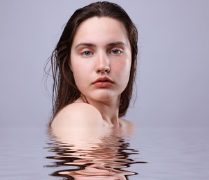 Image of Beautiful young woman with perfect skin against grey background. Her reflection in rippled water
