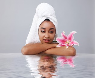 Image of Beautiful woman with perfect skin and lily flower against grey background. Her reflection in rippled water