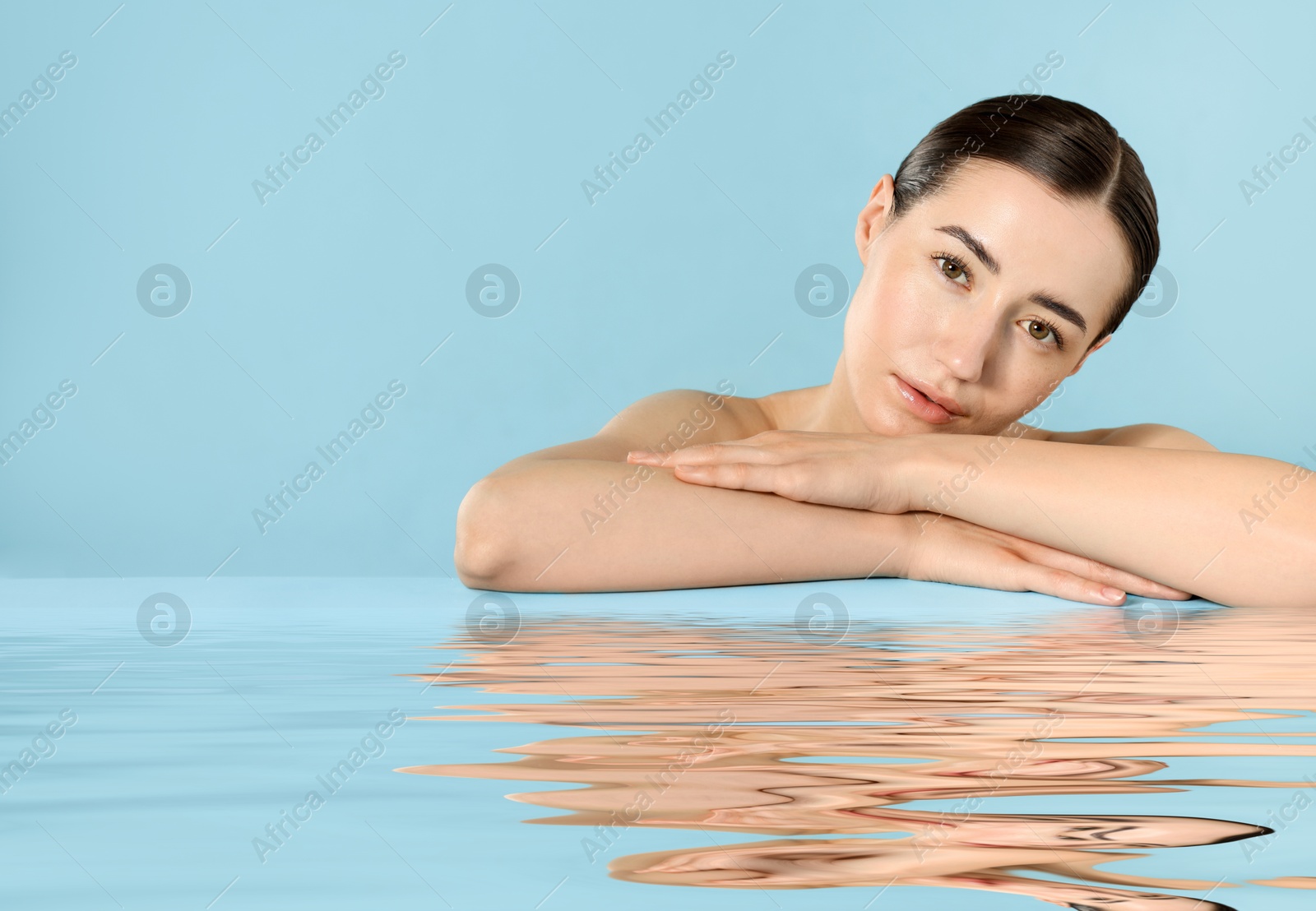 Image of Beautiful woman with perfect skin against light blue background. Her reflection in rippled water
