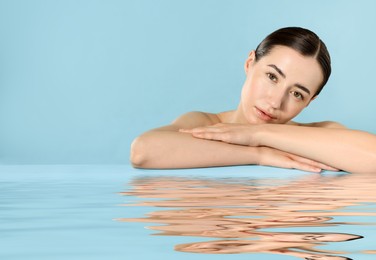 Image of Beautiful woman with perfect skin against light blue background. Her reflection in rippled water